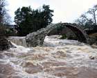 picture showing old packers bridge with the river in spate